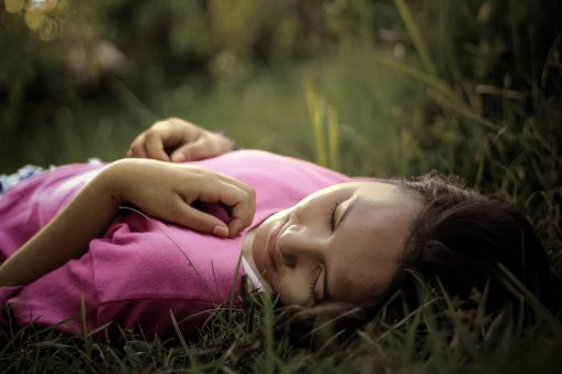 Vrouw ontspant op een ligbed in een groene tuin met kussens en planten rondom